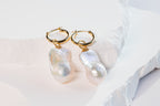 A pair of baroque pearl earrings with gold hoops, displayed on a white surface with a subtle background.